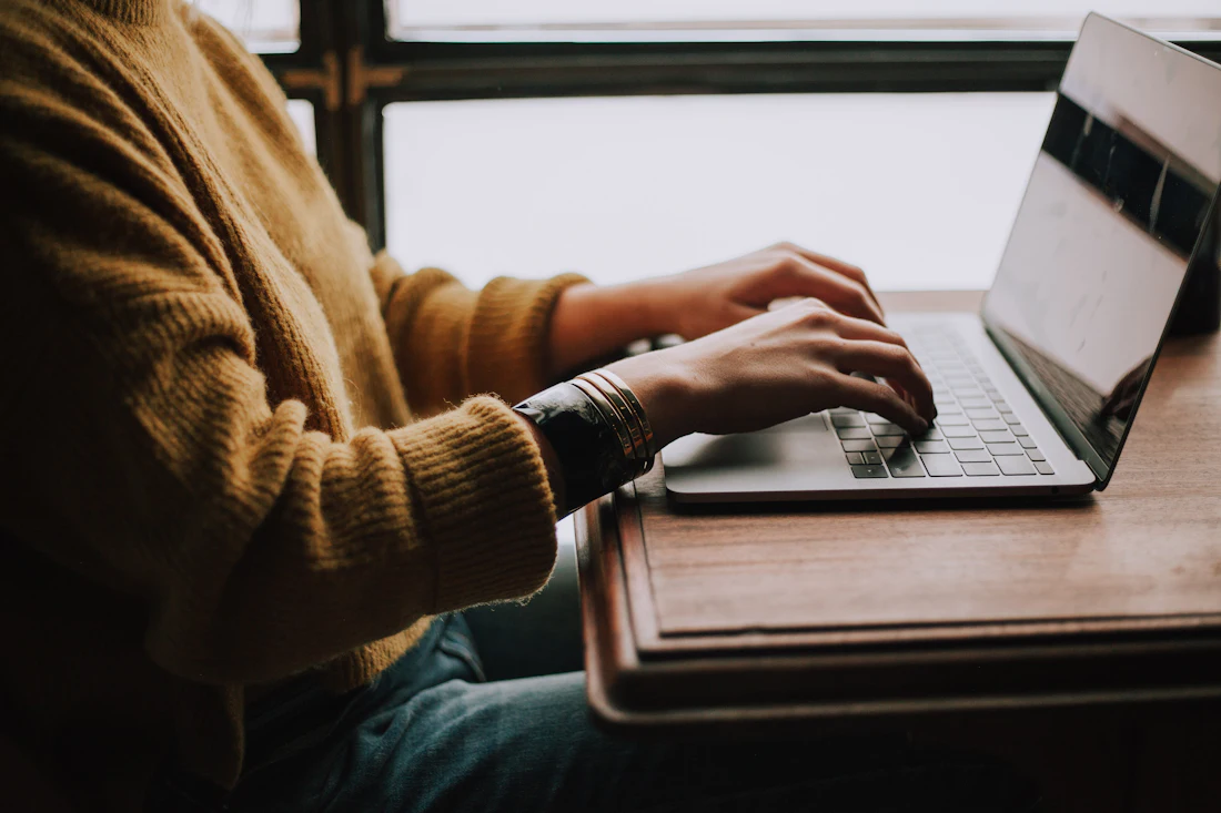 Manos escribiendo en una laptop sobre un escritorio de madera